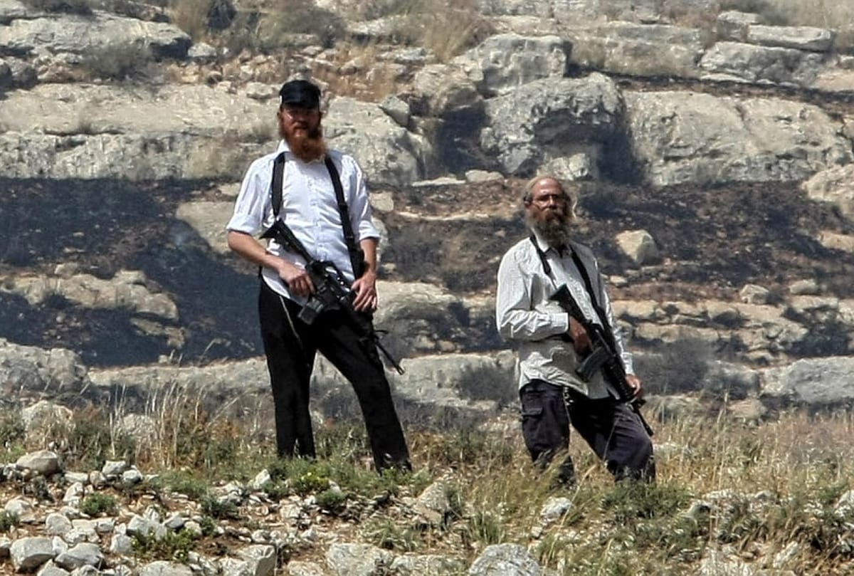 Colonos armados del asentamientoultraderechista de Yitzhar observan desde un acantilado la aldea palestina que se encuentra abajo. Foto: AFP